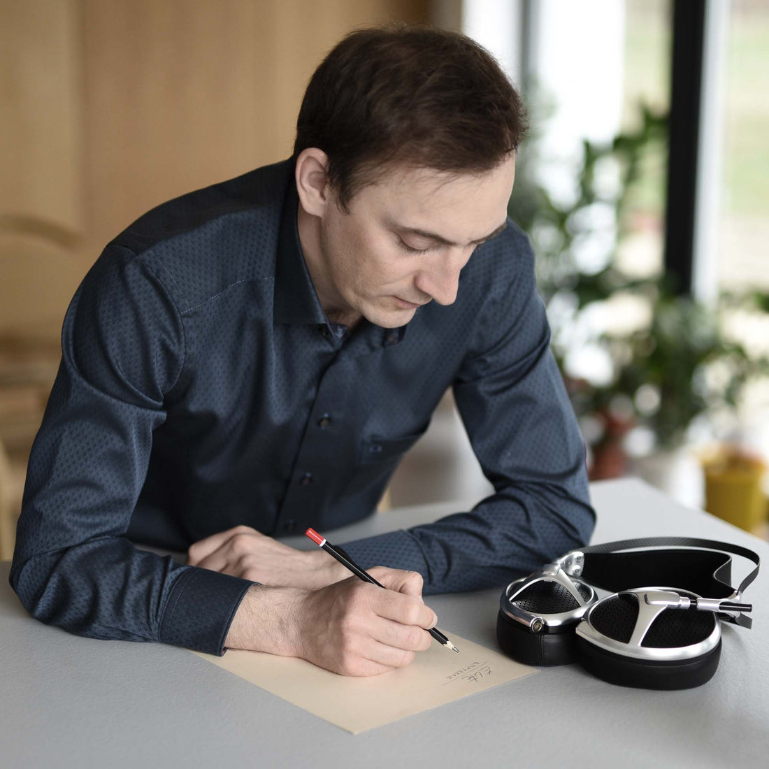 Antonio Meze at a writing table with a pair of silver Meze Elite headphones