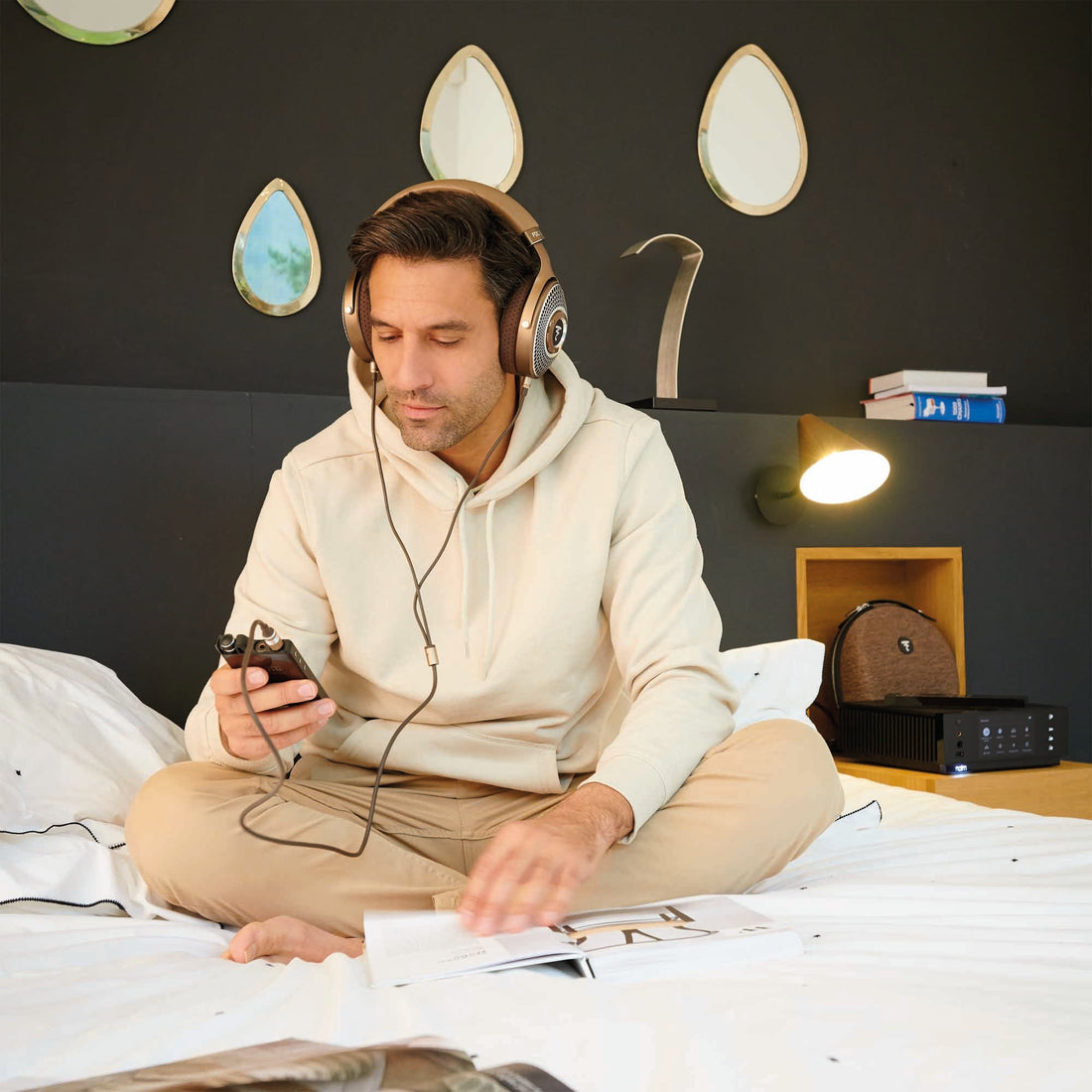 Man sitting on bed listening to Focal Clear Mg headphones with a portable music player