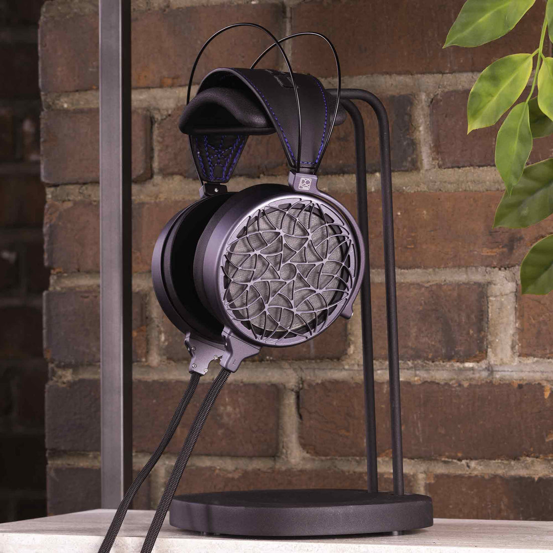Dan Clark Corina headphone hanging from metal stand in front of brick wall