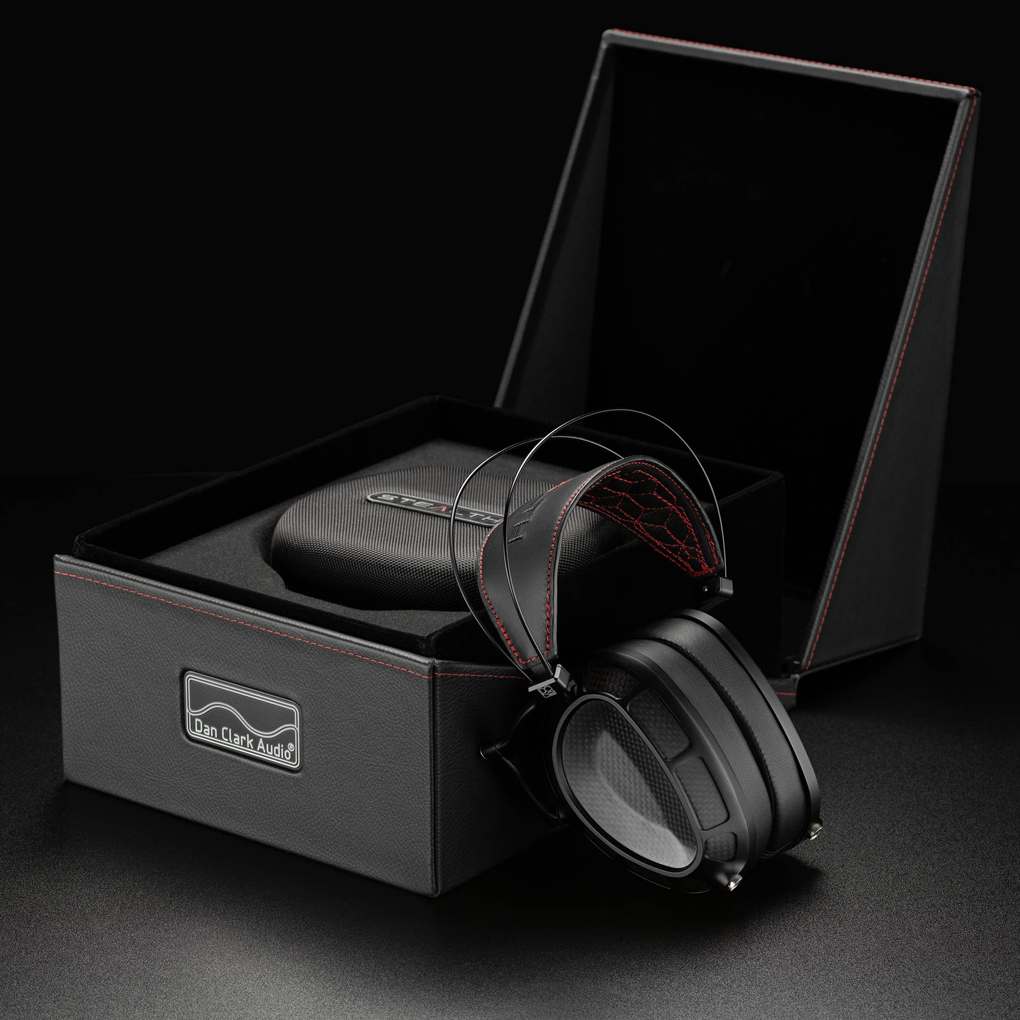 Dan Clark Stealth flagship closed-back headphone leaning against open presentation box with carrying case inside