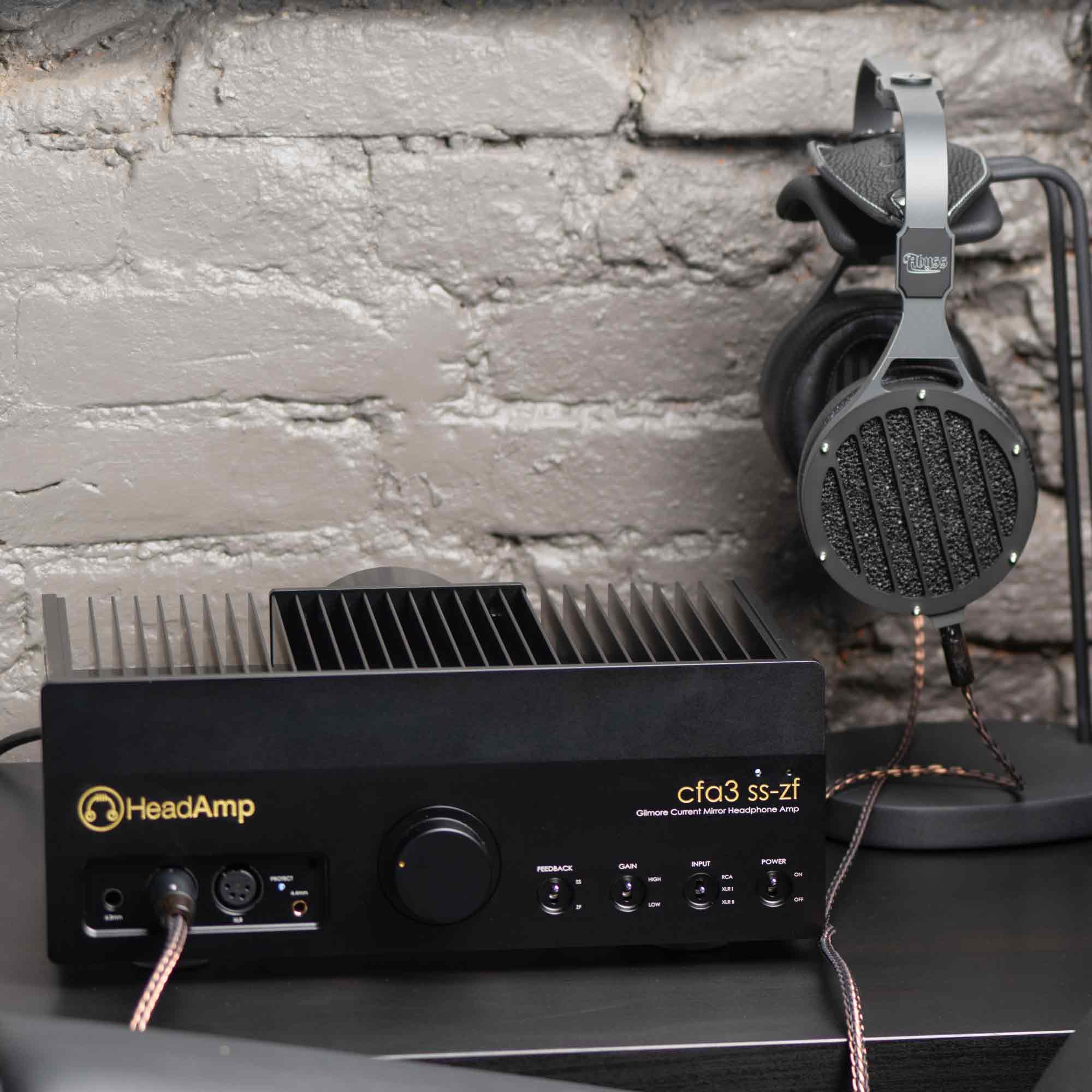 Abyss AB-1266 Phi TC headphones hanging on a stand connected to a black HeadAmp cfa3 ss-zf amplifier against a textured wall