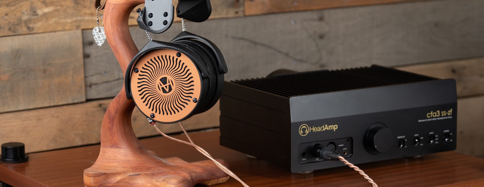 Pair of wooden-accented over-ear headphones hanging on a wooden stand next to a black audio amplifier on wood surface