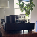 Side view of the HeadAmp Grand Cayman DHT Electrostatic Amp (Pre-Order Deposit) with tubes on wooden table near window light