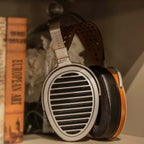 HIFIMAN HE1000 Stealth Open-Back Planar Magnetic Headphones resting on a shelf next to art books in warm lighting