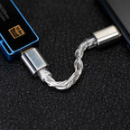 Close-up of the iBasso CB18 USB-C to USB-C OTG Cable, showing its braided design and metal connectors connected between a blue Hi-Res Audio device and a black electronic device on a textured black surface.