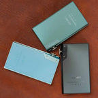 Three iBasso DX180 Digital Audio Players in black, green, and blue colors placed on brown leather surface
