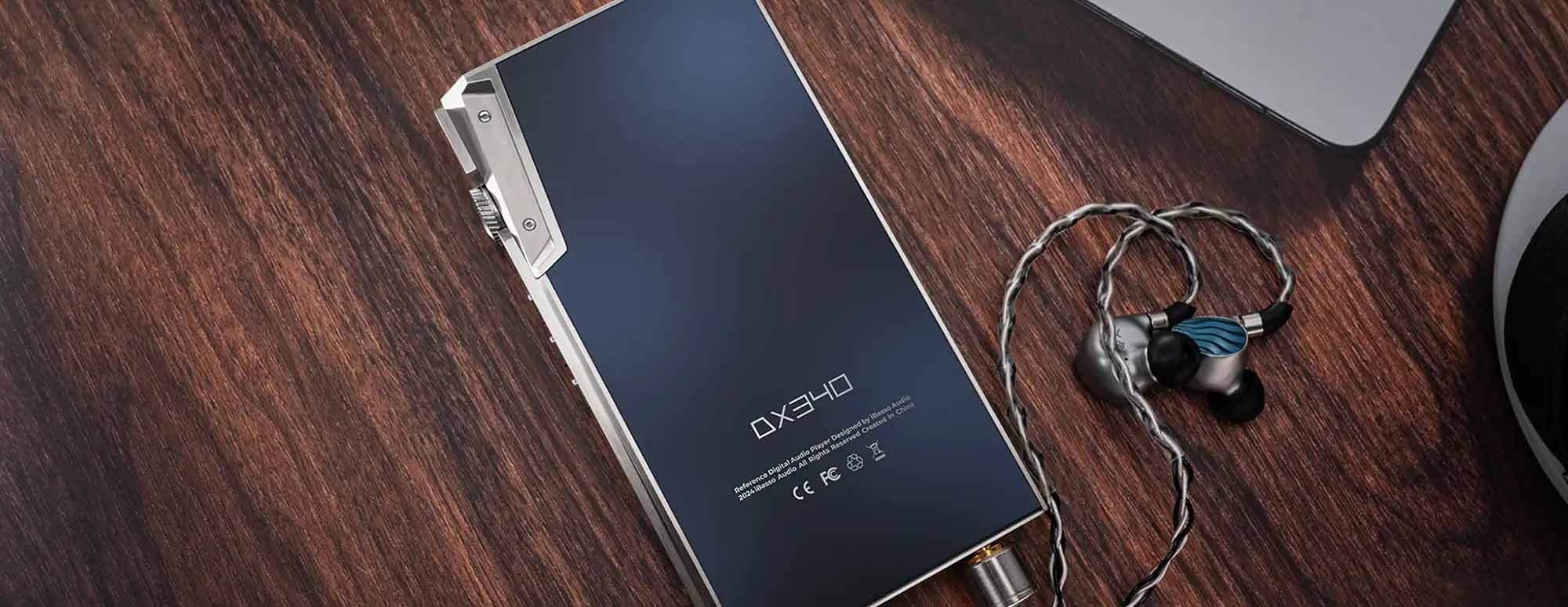 Portable digital audio player with connected in-ear monitors resting on a dark wooden surface near a laptop corner