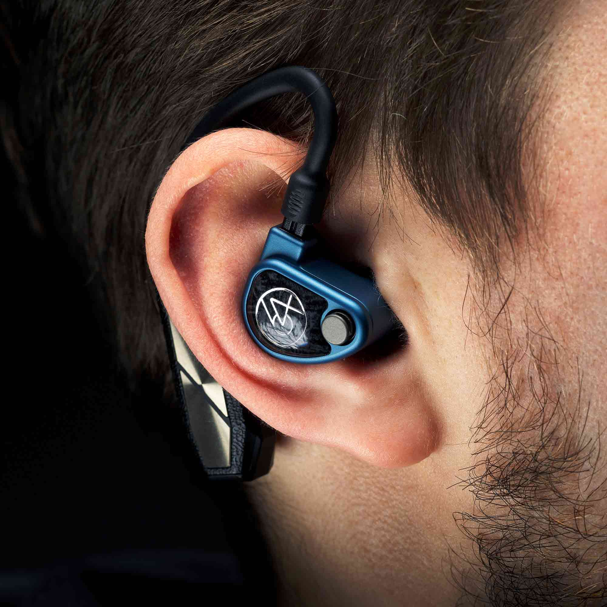 Close-up of iFi Audio GO Pod Wearable Bluetooth DAC/Amp fitted in ear with black ear hook on dark background