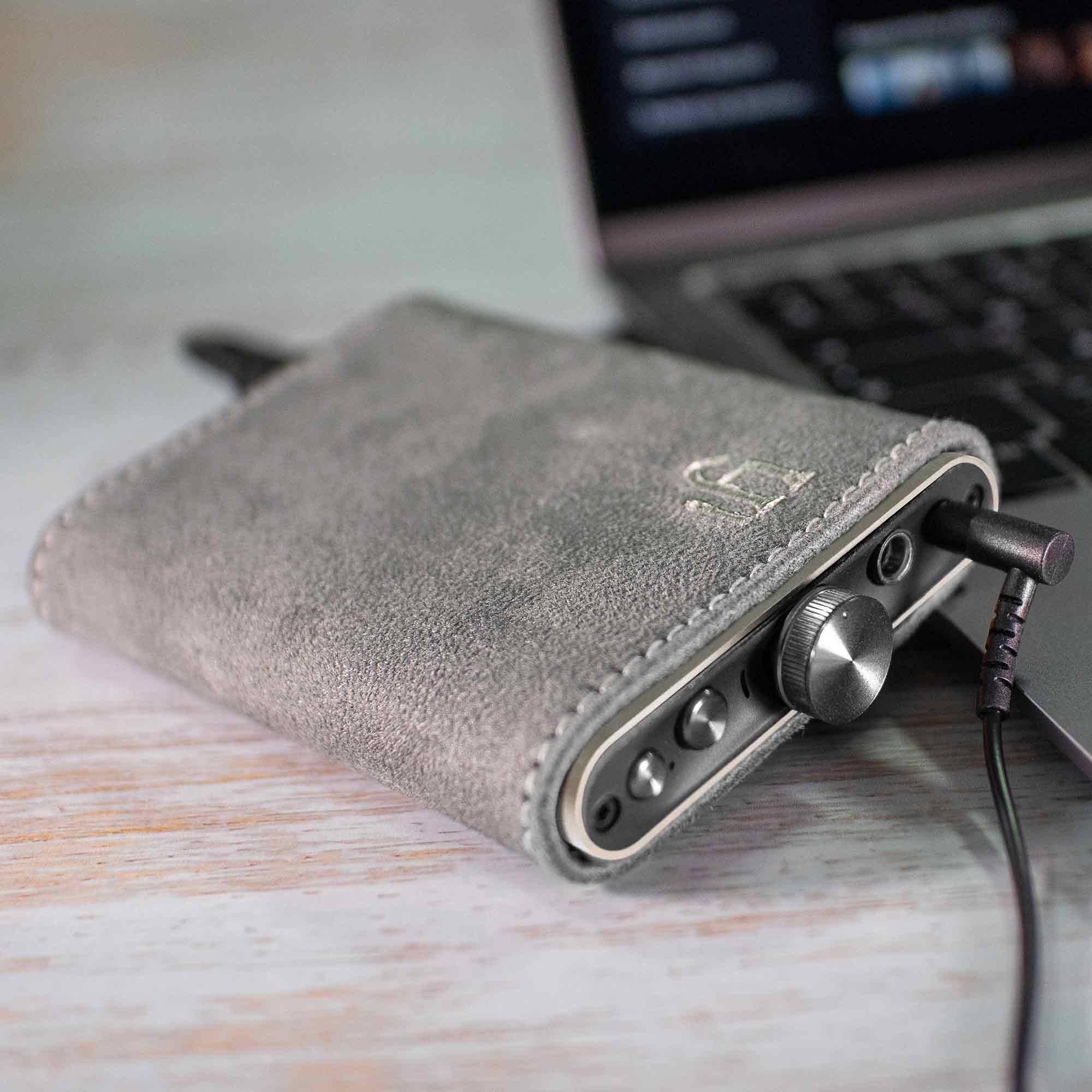 iFi Audio Hip Case for Hip-DAC Series in gray suede protecting a compact DAC with volume knob and headphone jack connected to a laptop