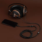Meze 105 SILVA Dynamic Open-Back Headphones with wood ear cups connected to a smartphone on a brown surface