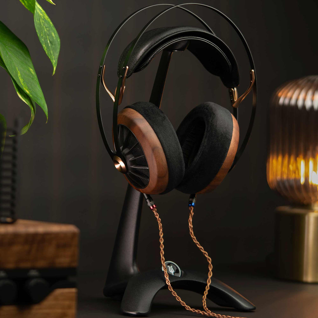 Meze Manta Headphone Stand holding wood and black headphones with braided cable in ambient lighting setting