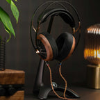 Meze Manta Headphone Stand holding wood and black headphones with braided cable in ambient lighting setting