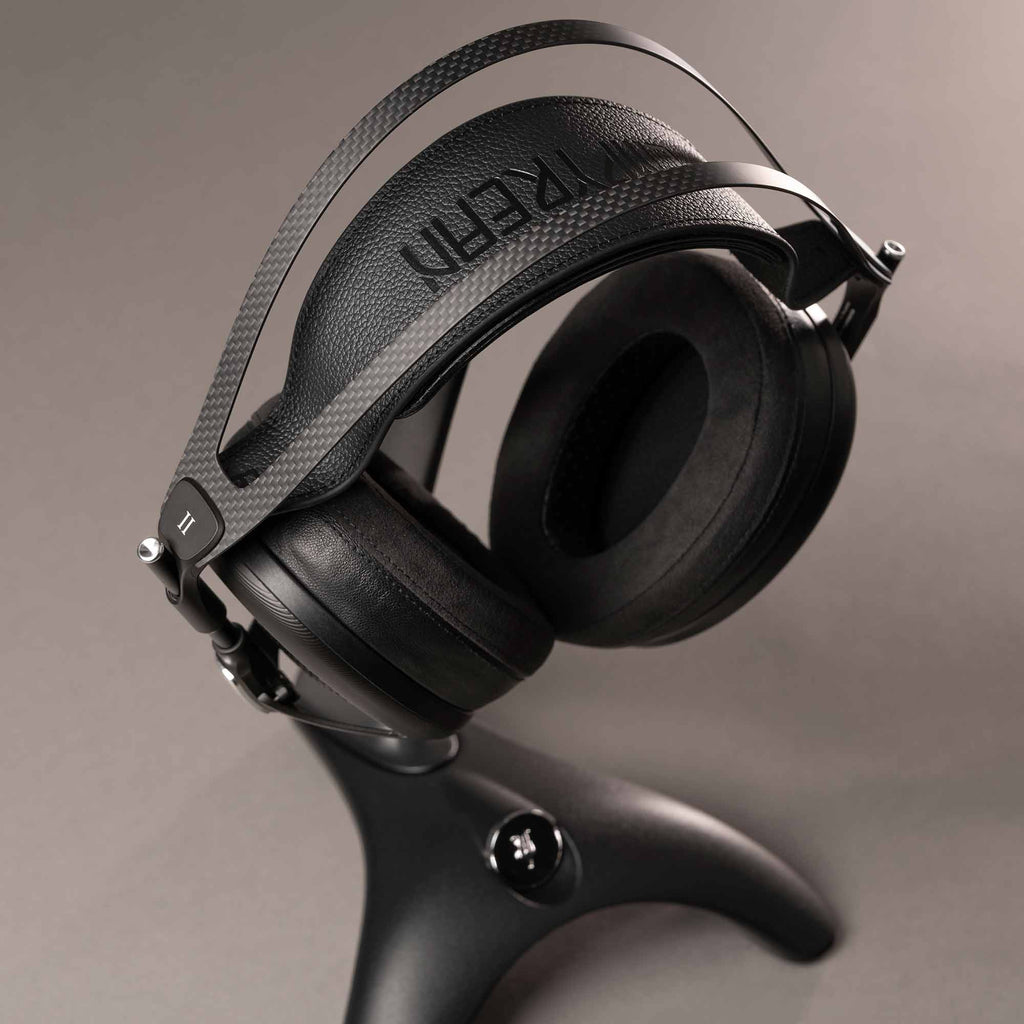 Meze Manta Headphone Stand holding black headphones with carbon fiber headband and padded ear cups on gray background