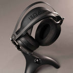 Meze Manta Headphone Stand holding black headphones with carbon fiber headband and padded ear cups on gray background