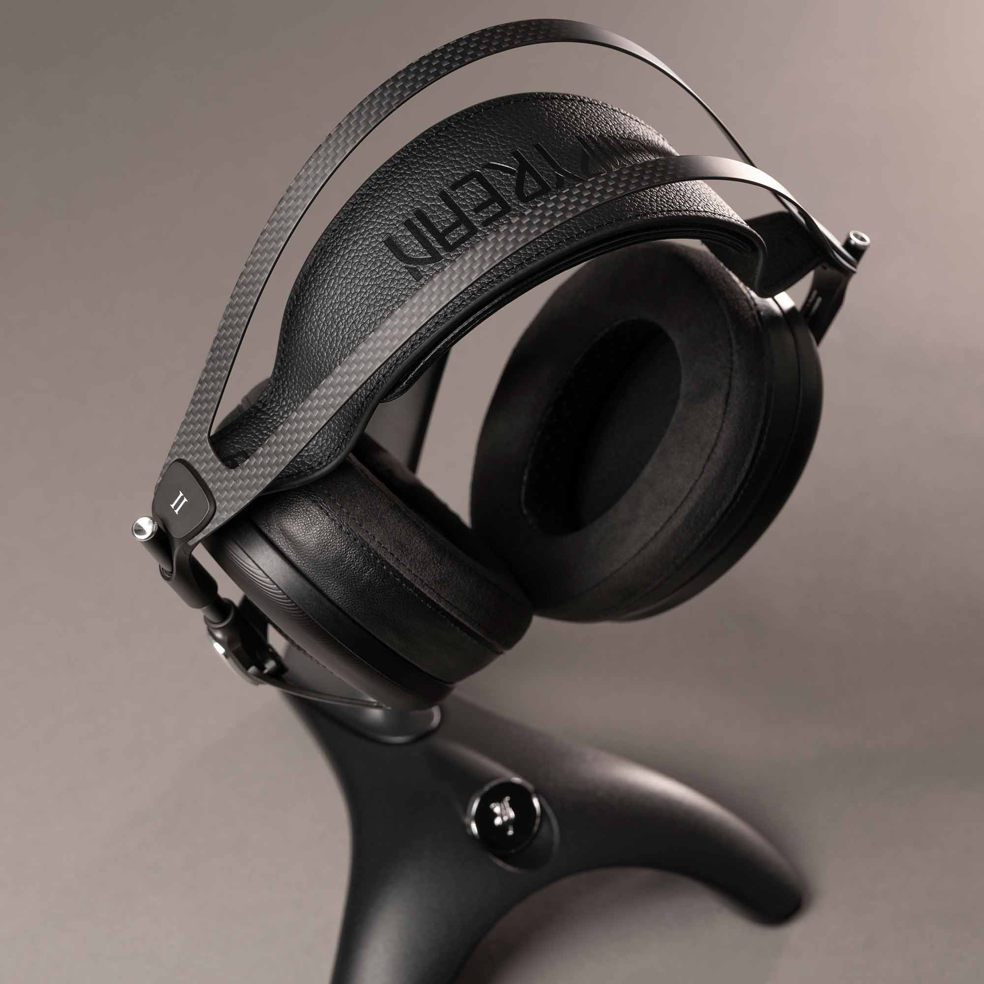 Meze Manta Headphone Stand holding black headphones with carbon fiber headband and padded ear cups on gray background