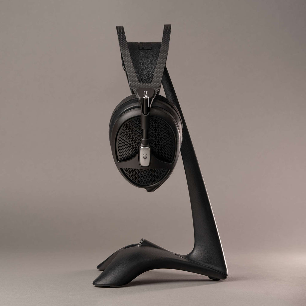 Meze Manta Headphone Stand holding black headphones with carbon fiber texture and sleek curved base on neutral background