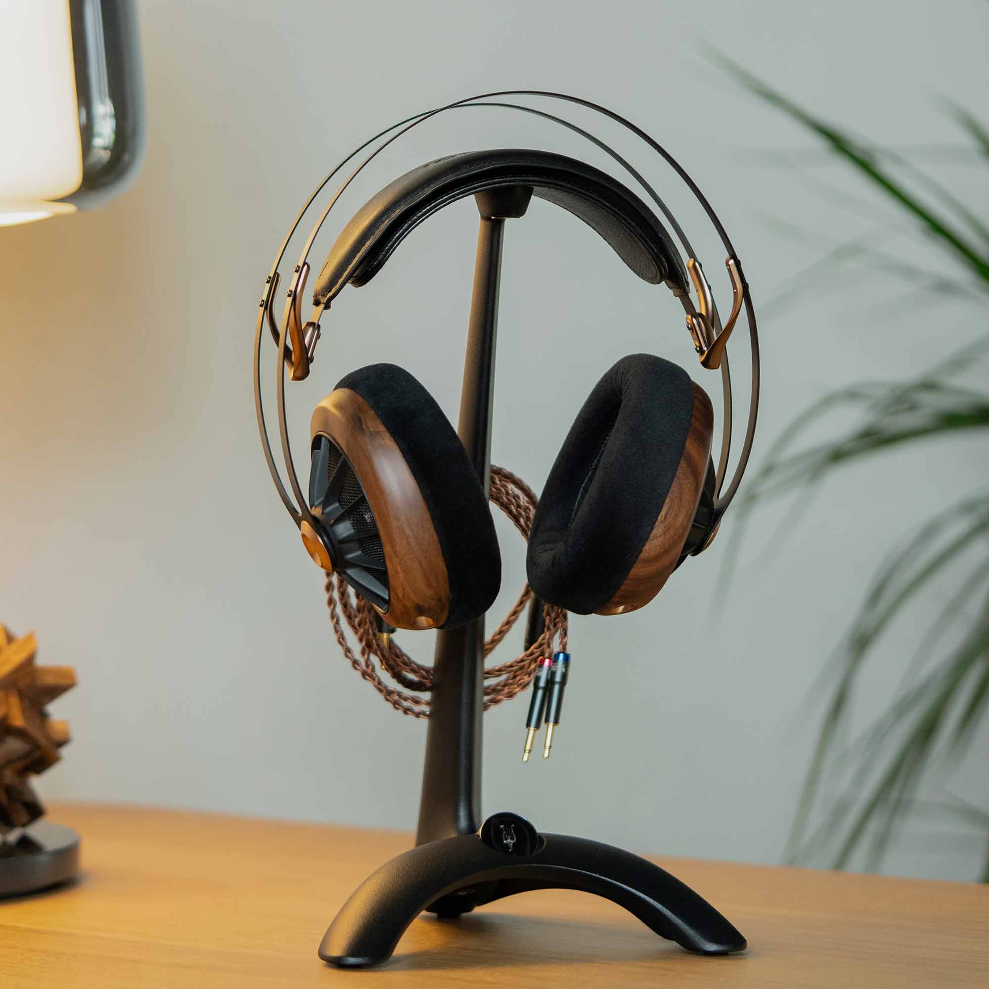 Meze Manta Headphone Stand with premium headphones featuring wooden ear cups and braided cable on wooden surface