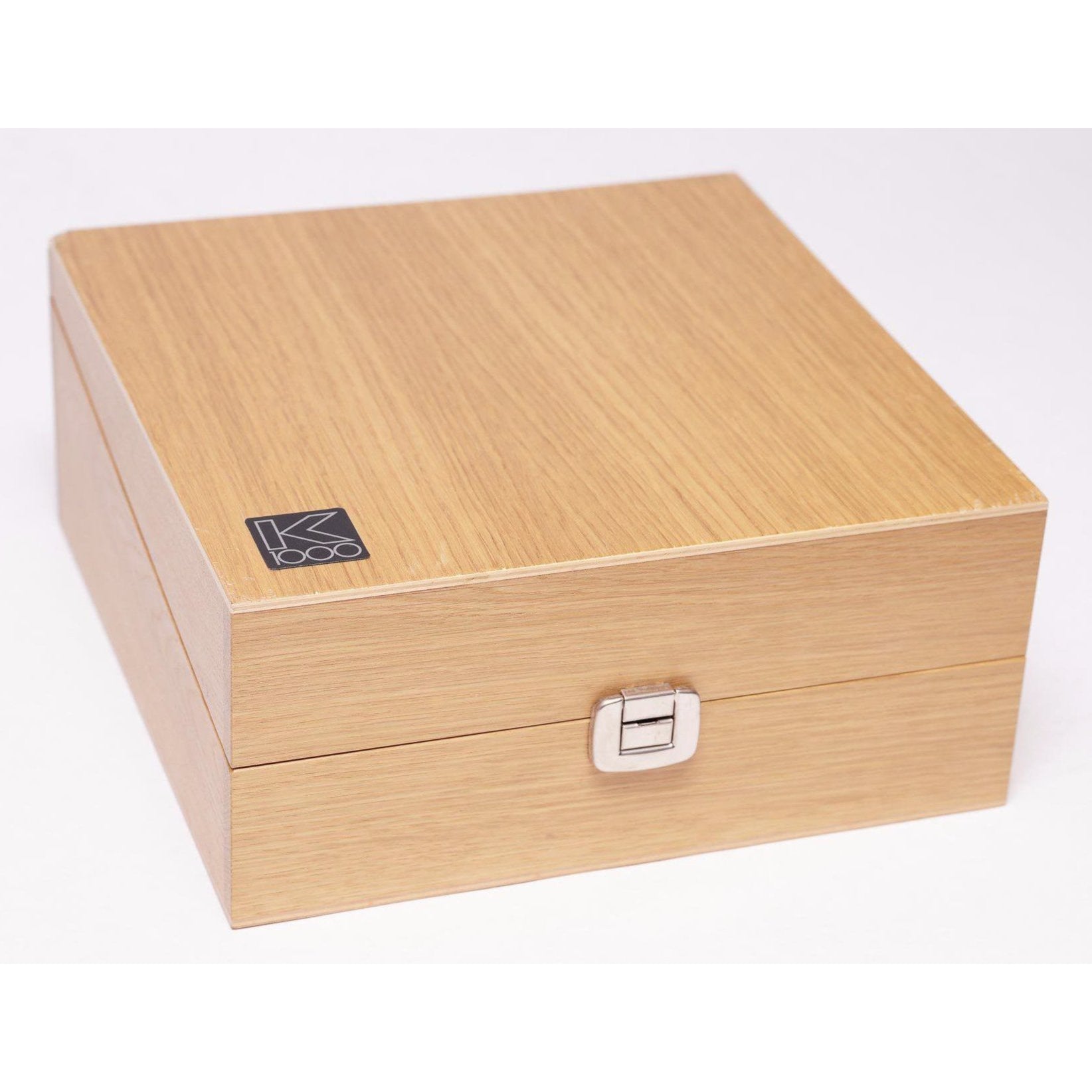 Closed light wood storage box with a metal clasp and AKG K1000 logo on the top left corner on white background