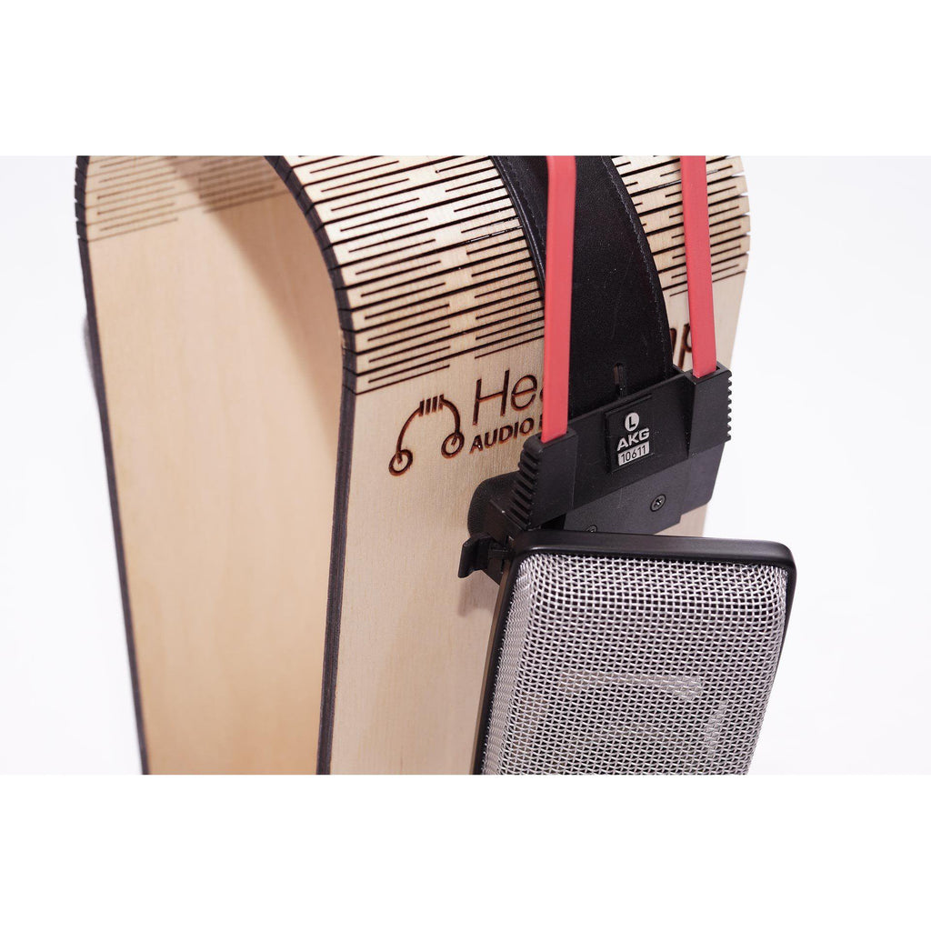 Side view of AKG K1000 open back headphones resting on a wooden headphone stand with red headband straps