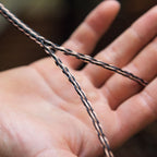 Close-up of a hand holding the braided Kimber Kable Axios Copper Headphone Cable showing copper and black strands