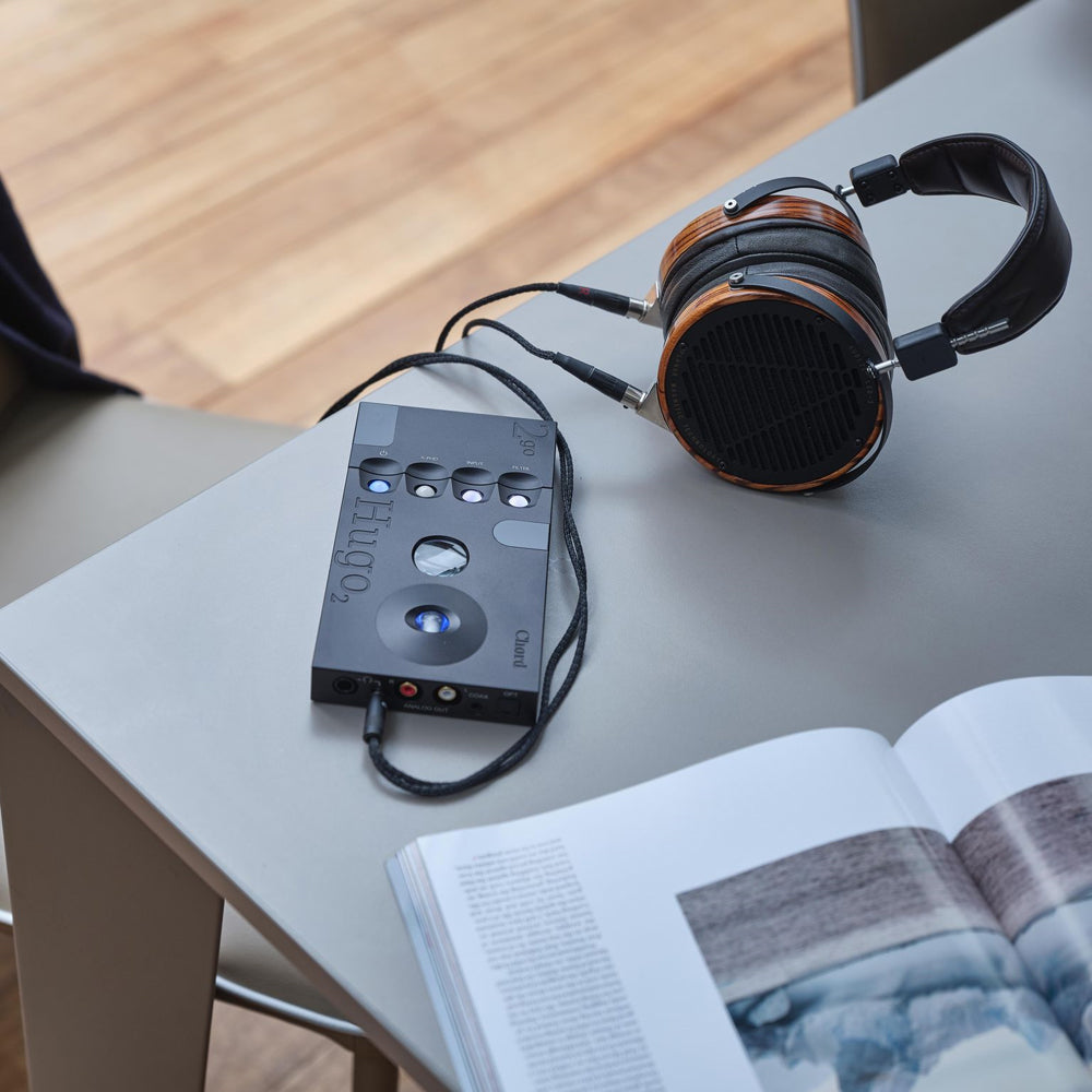 Chord 2Go Wireless Streamer connected to Hugo 2 DAC and wooden over-ear headphones on a gray table next to an open book