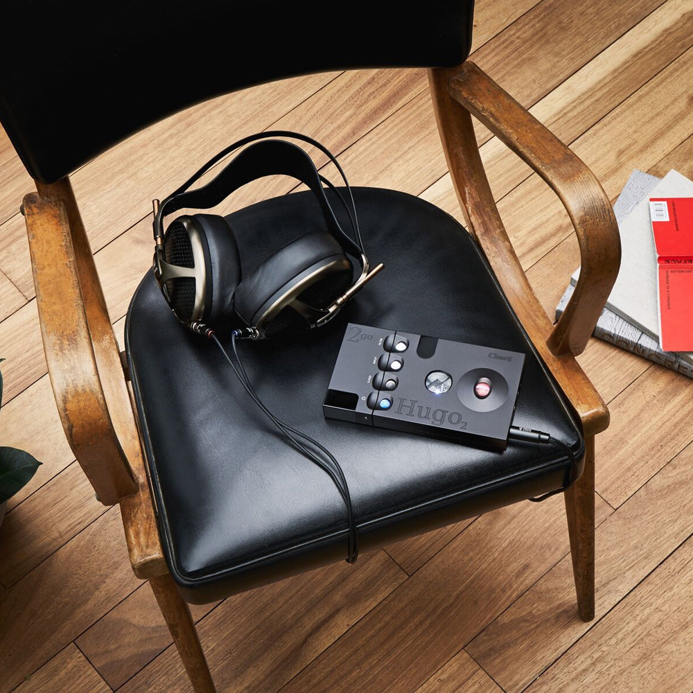 Chord 2Go Wireless Streamer placed on black chair seat with wired headphones and wooden armrests nearby